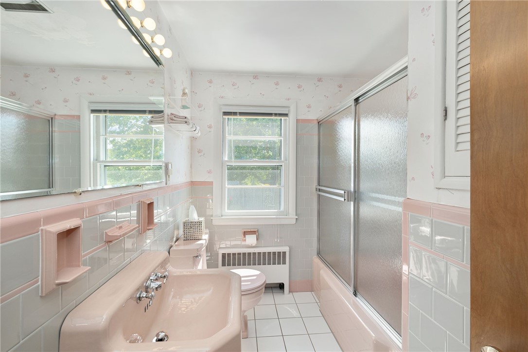 Bathroom with pale pink tile, a long vanity sink, and a tub with sliding glass doors.