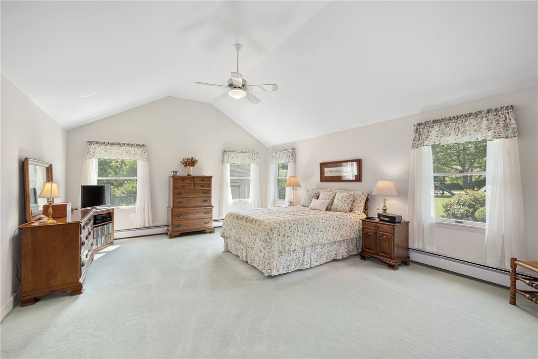 Spacious bedroom with a vaulted ceiling, floral bedding, and windows overlooking trees.