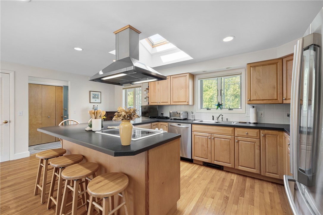 Kitchen with a large cooktop island, four stools, wood cabinetry, and a skylight.