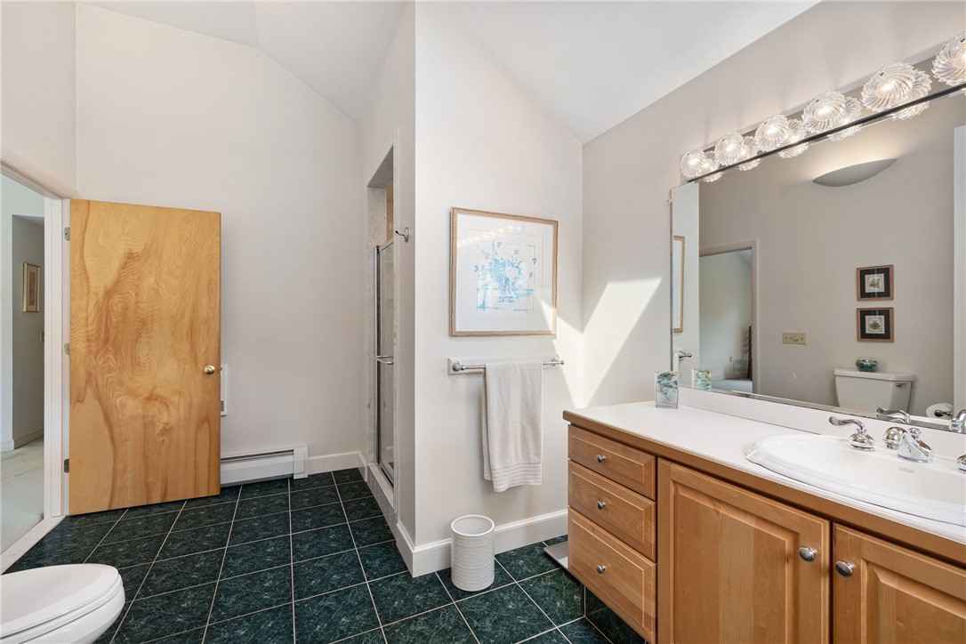 Bathroom with a wood vanity, globe-lit mirror, dark green tile floor, and glass shower.