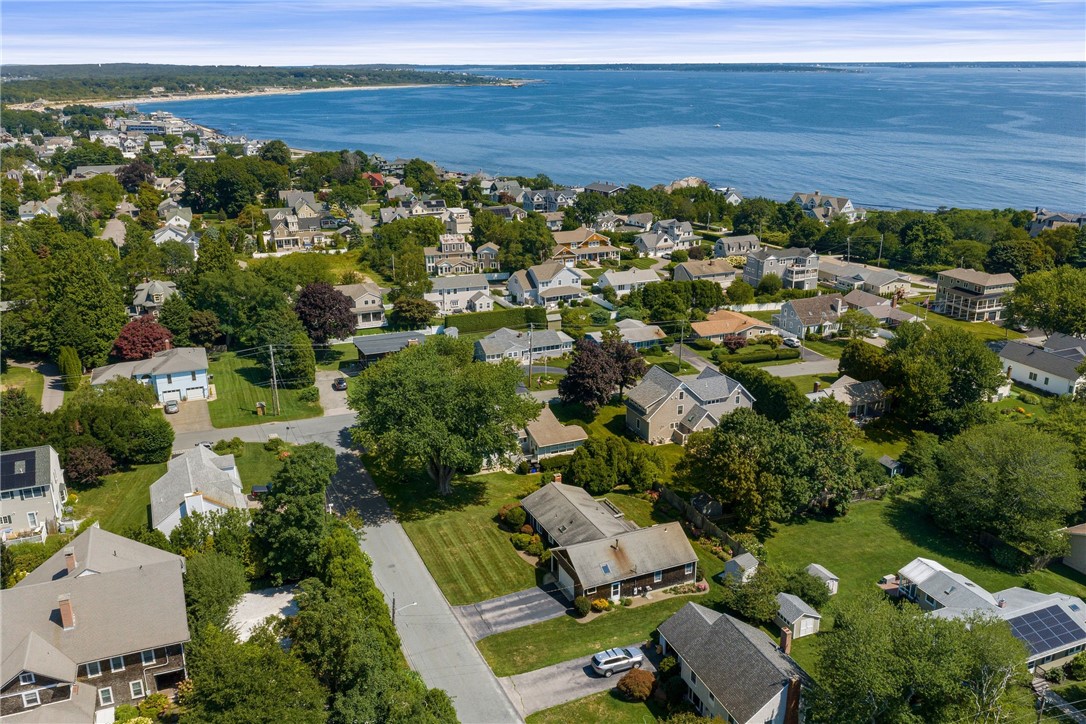 Aerial view of a coastal neighborhood beside a broad bay, with tree-lined streets and homes.