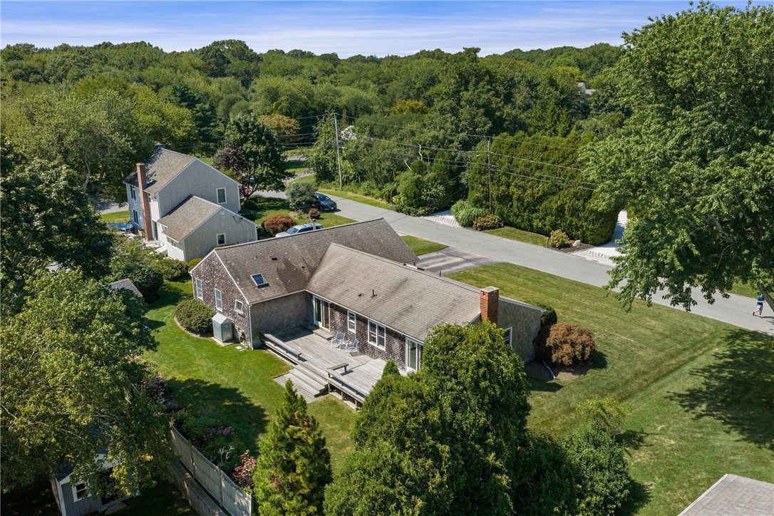 Aerial view of a shingle-style home with a wide wooden deck and tree-lined lawn.