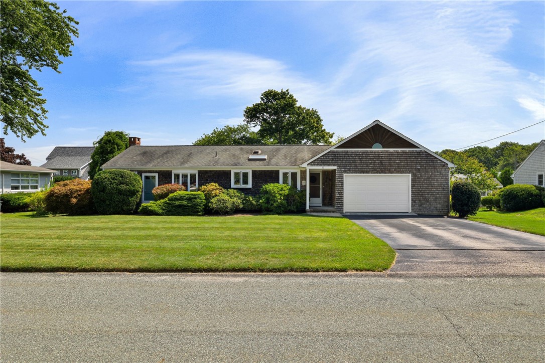 Single-story shingle-sided home with a white garage door, landscaped lawn, and driveway.