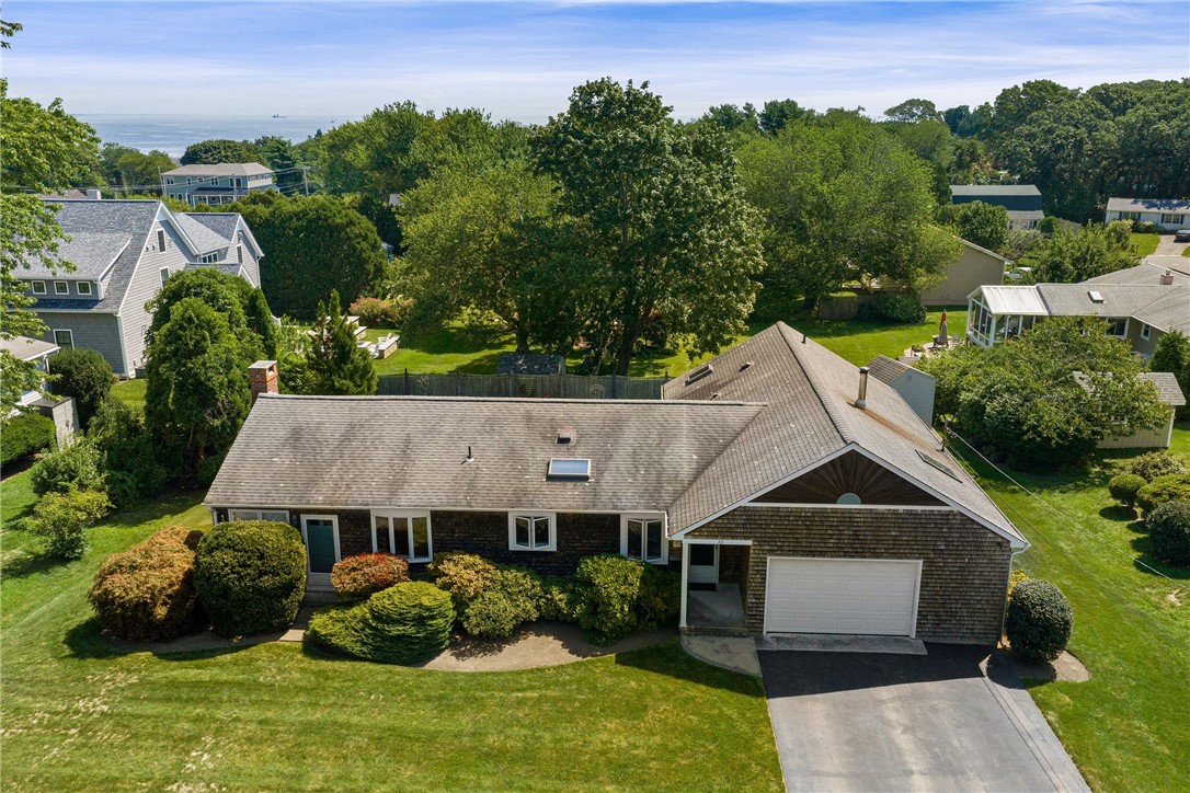 Aerial view of a shingle-sided home with an attached garage and ocean visible beyond the trees.