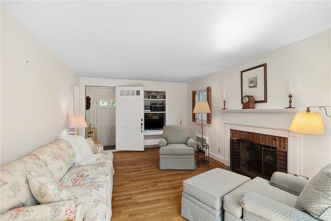Living room with a brick-surround fireplace, hardwood floors, floral sofa, and built-in television shelving.