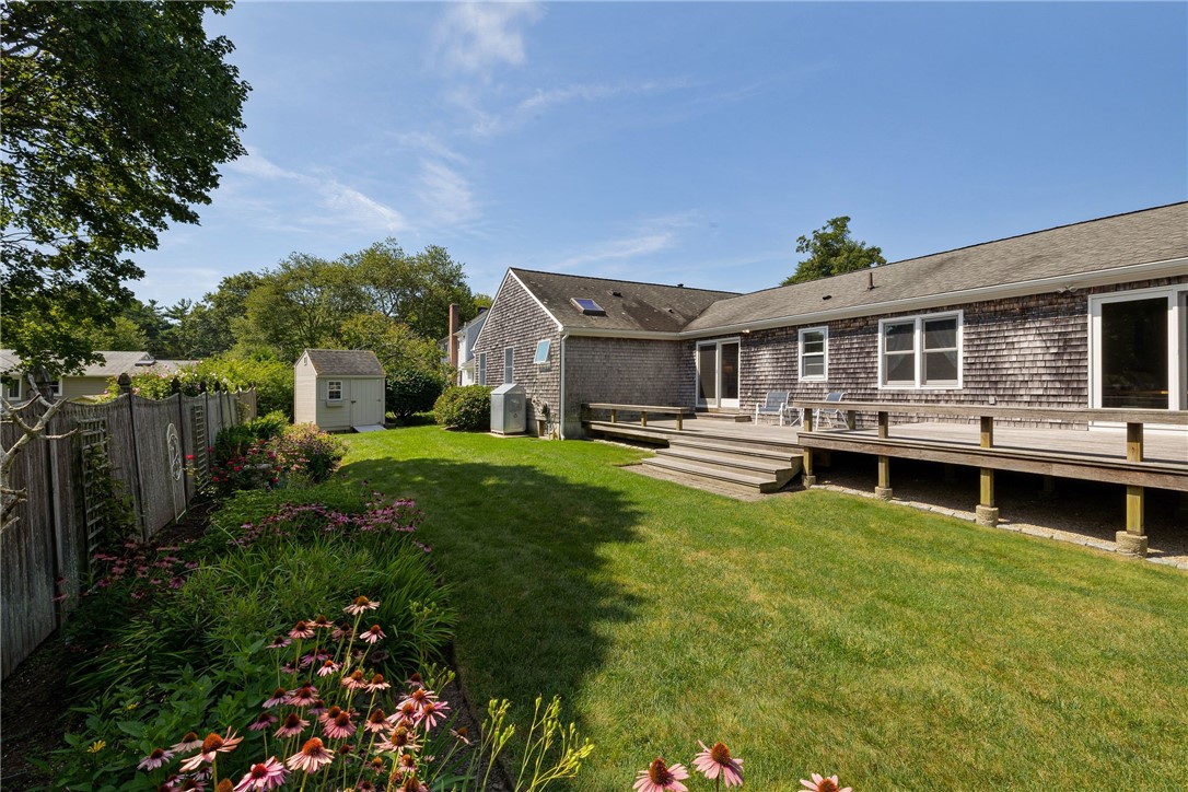 Shingled home with a raised wooden deck overlooking a green lawn and flower beds.