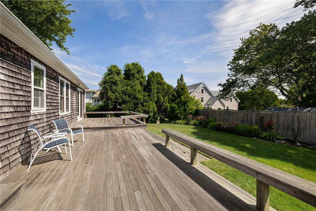 Wide wooden deck beside a shingle-sided house, overlooking a fenced lawn and garden.