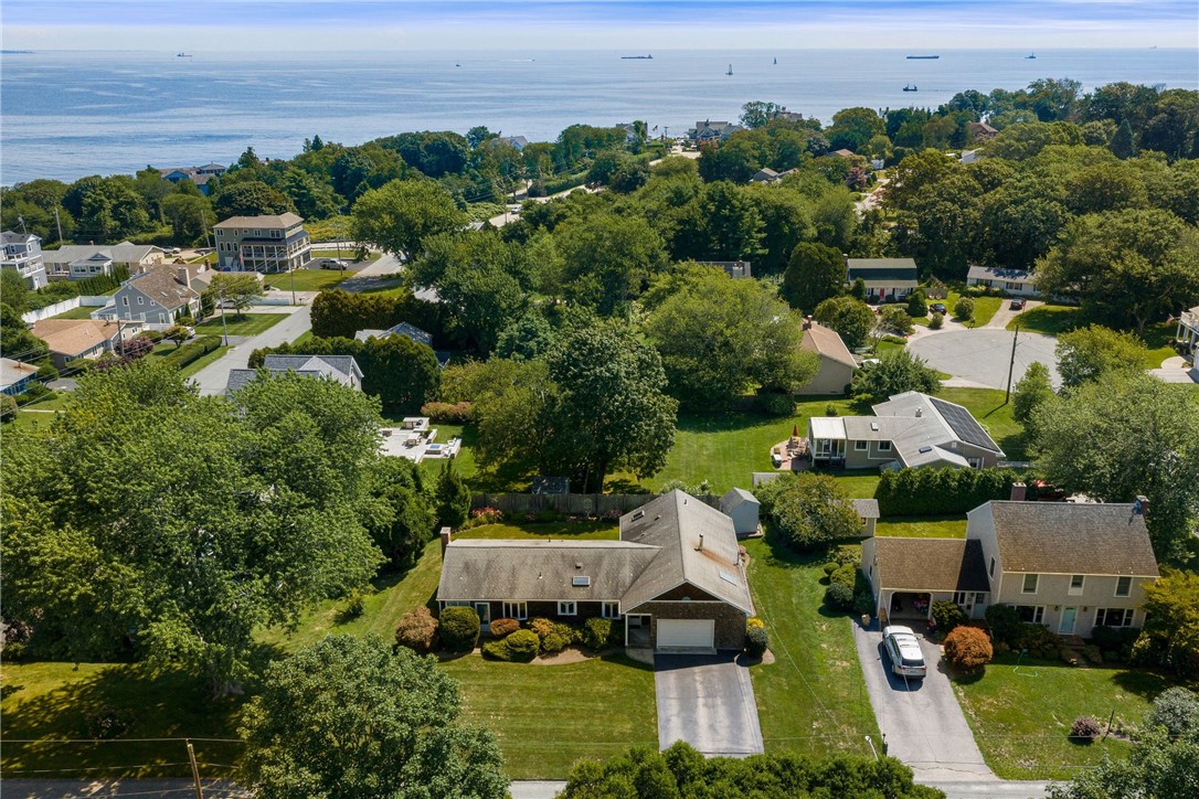 Aerial view of coastal homes and green lawns, with boats on the ocean in the distance.