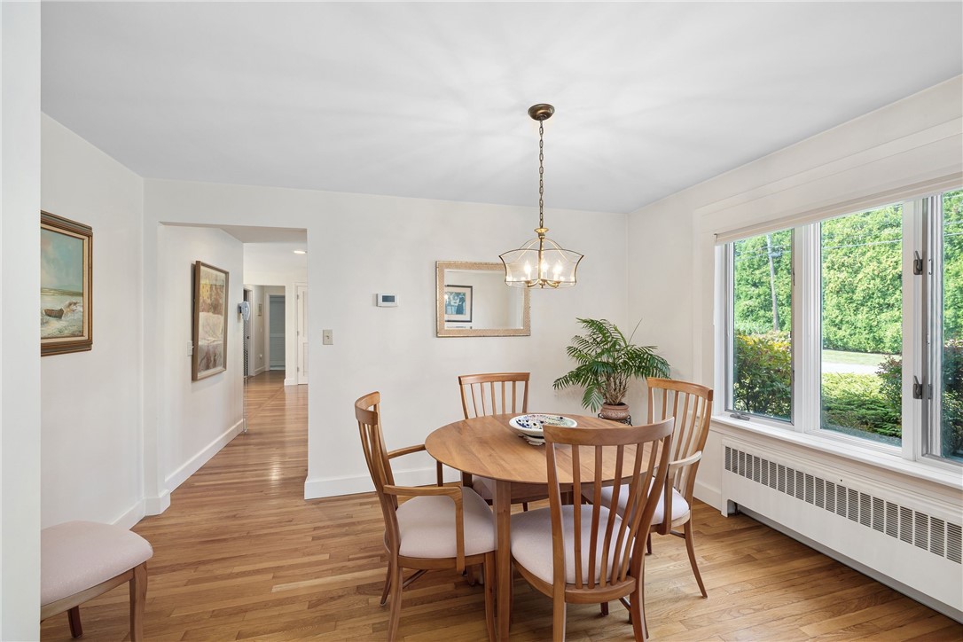 Dining room with a round wooden table, hardwood floors, and large windows overlooking greenery.
