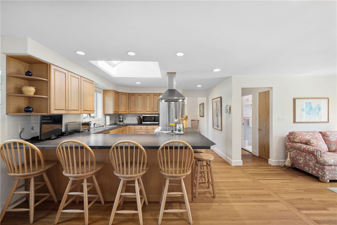 Open kitchen with a dark island, wooden stools, honey-toned cabinets, and a skylight beside a floral sofa.