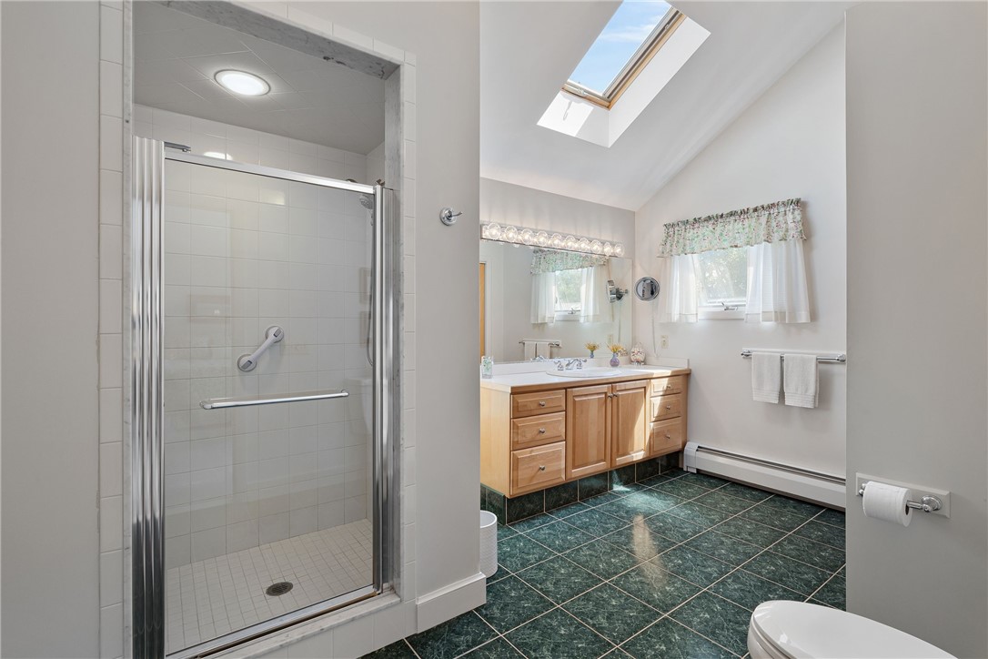 Bathroom with a glass shower, wood vanity, dark green tile floor, and skylight.