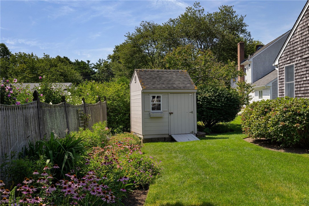 Backyard garden shed beside a green lawn, flowering beds, and a wooden fence.