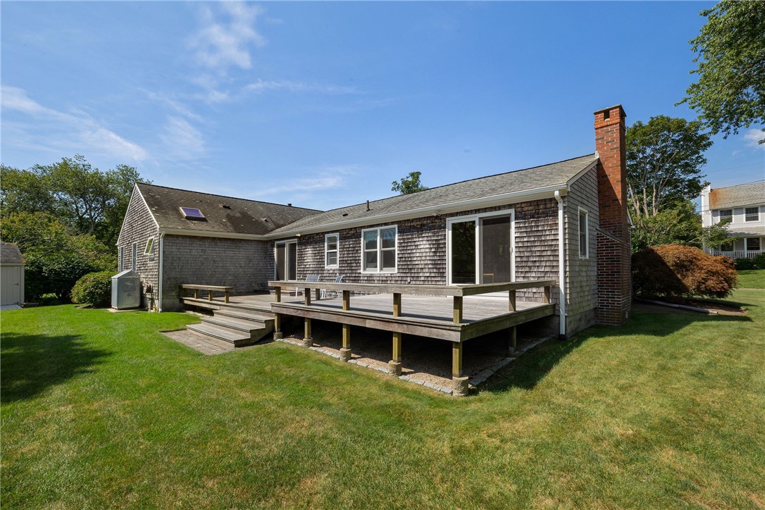 Cedar-shingle home with a raised wooden deck and brick chimney behind a green lawn.