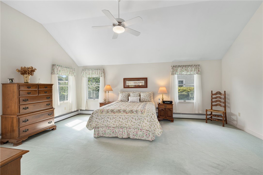 Bedroom with a vaulted ceiling, floral bedding, ceiling fan, and three windows.