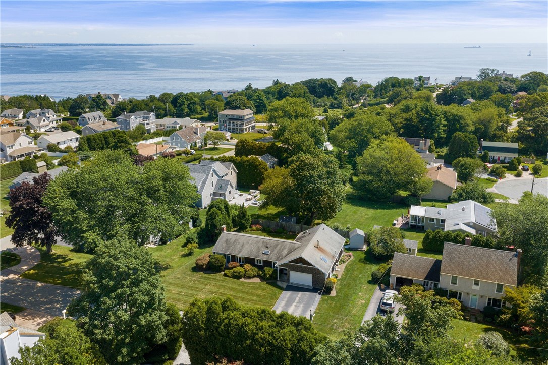 Aerial view of a coastal neighborhood with homes, leafy streets and ocean beyond.