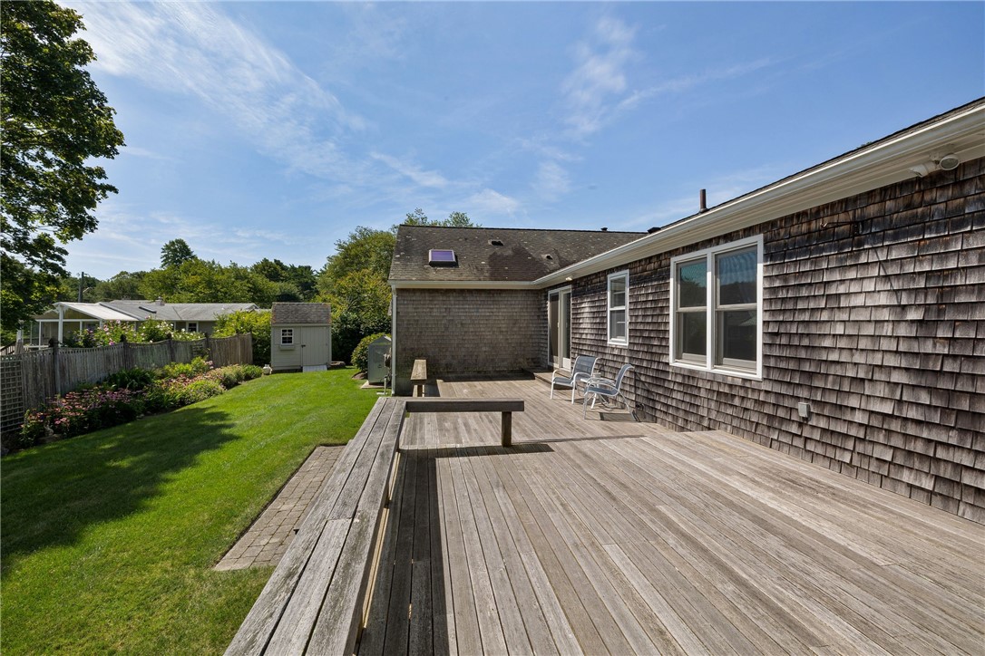 Shingled home with a spacious wooden deck overlooking a green lawn and flower garden.