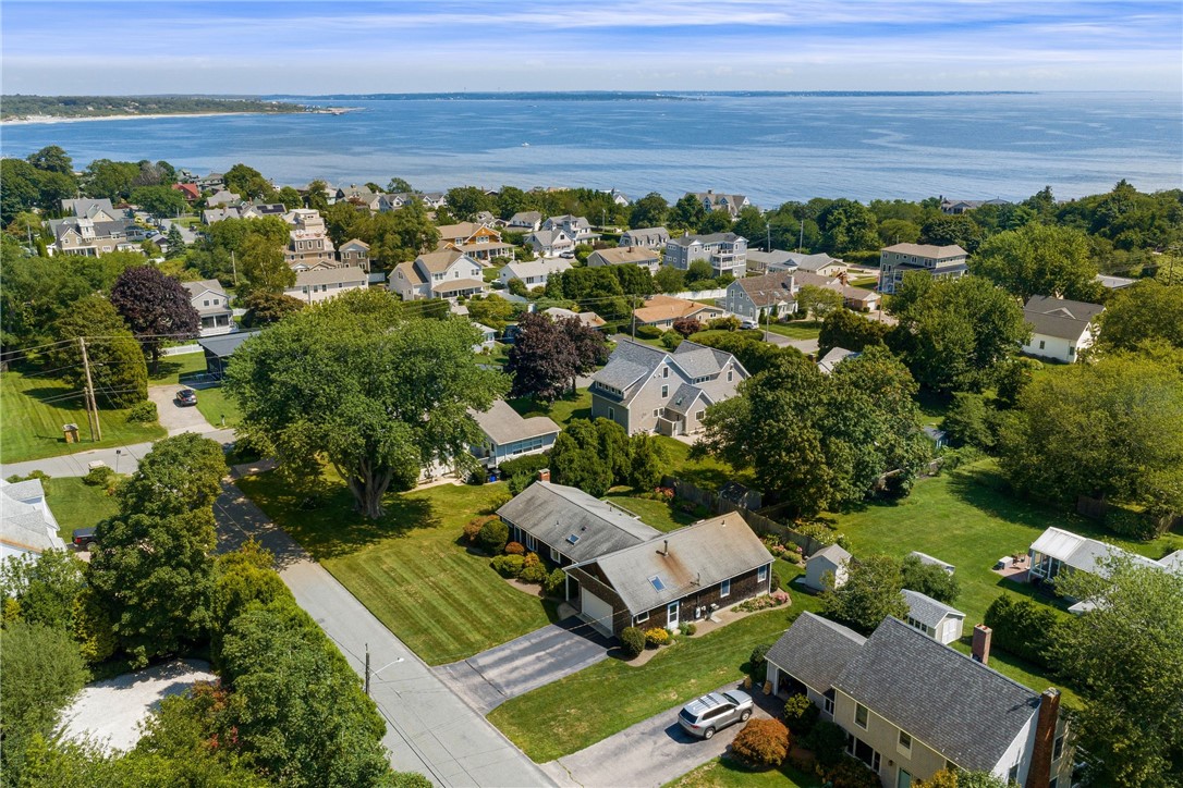 Coastal neighborhood aerial with tree-lined streets, detached homes, and ocean beyond.