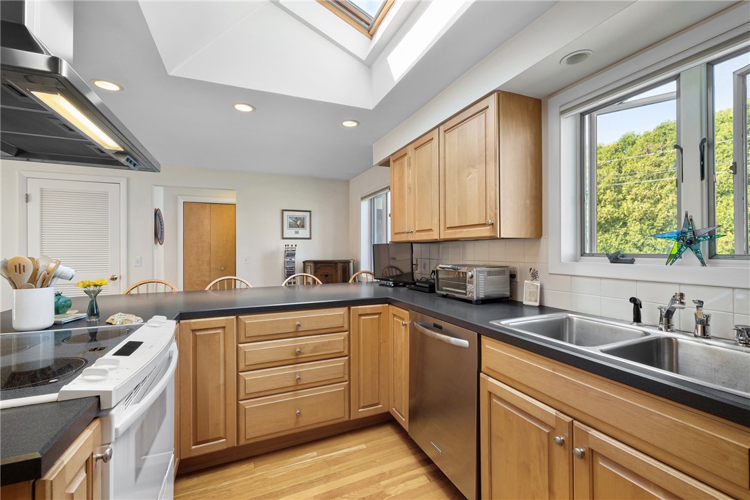 Kitchen with wood cabinetry, stainless steel appliances, a double sink, and a skylight.