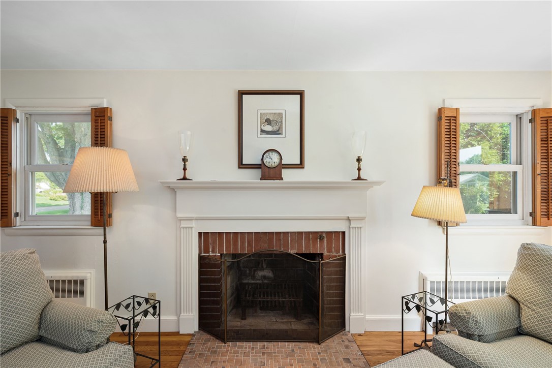Living room with a brick fireplace, white mantel, shuttered windows, and patterned armchairs.