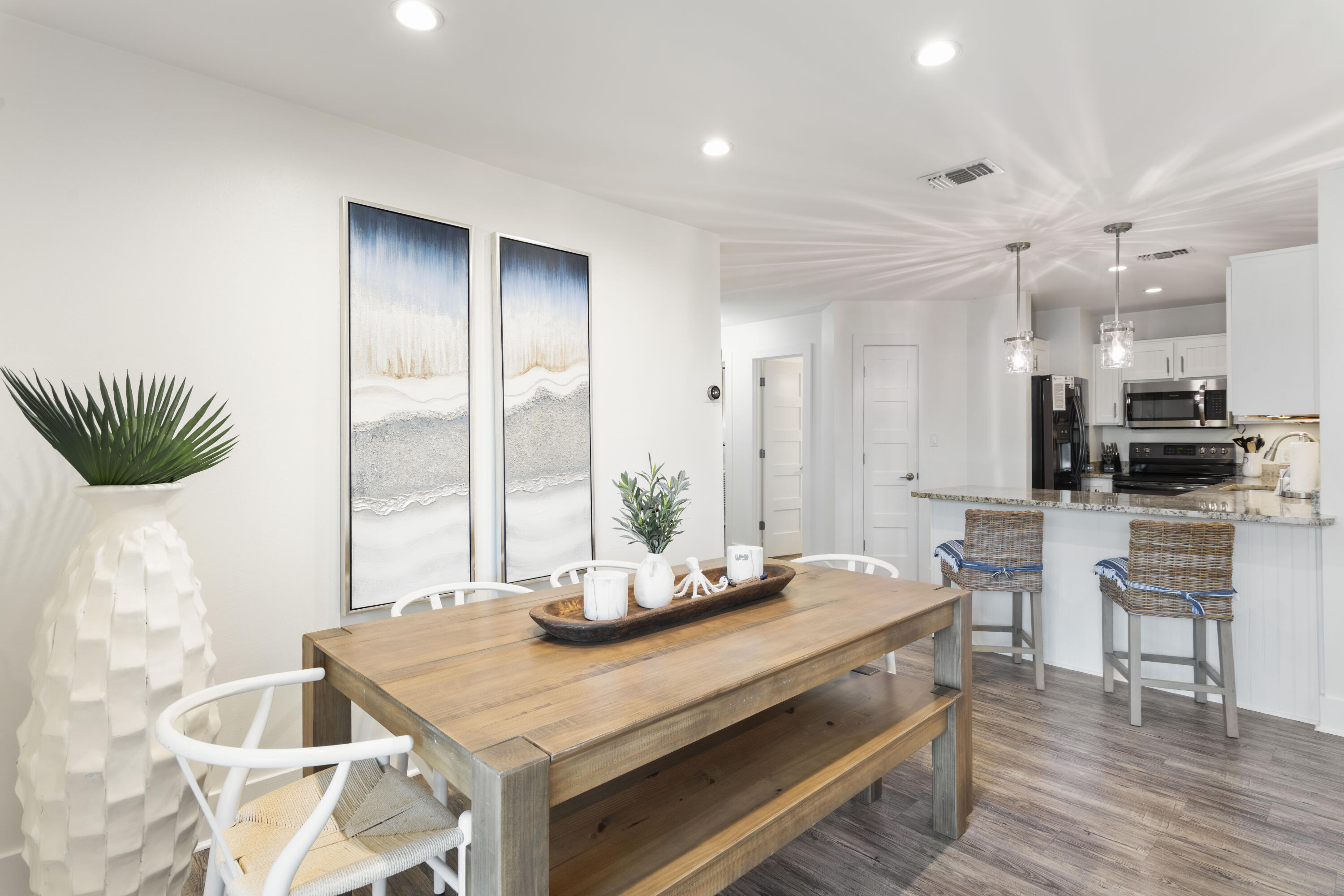 Dining area with a large wooden table opening to a bright kitchen and island.
