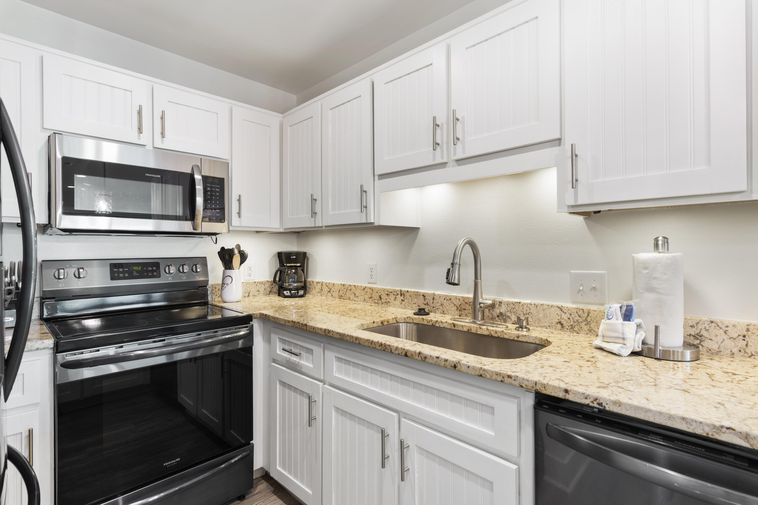 Kitchen with white paneled cabinets, granite counters, stainless sink, and black electric range and microwave.