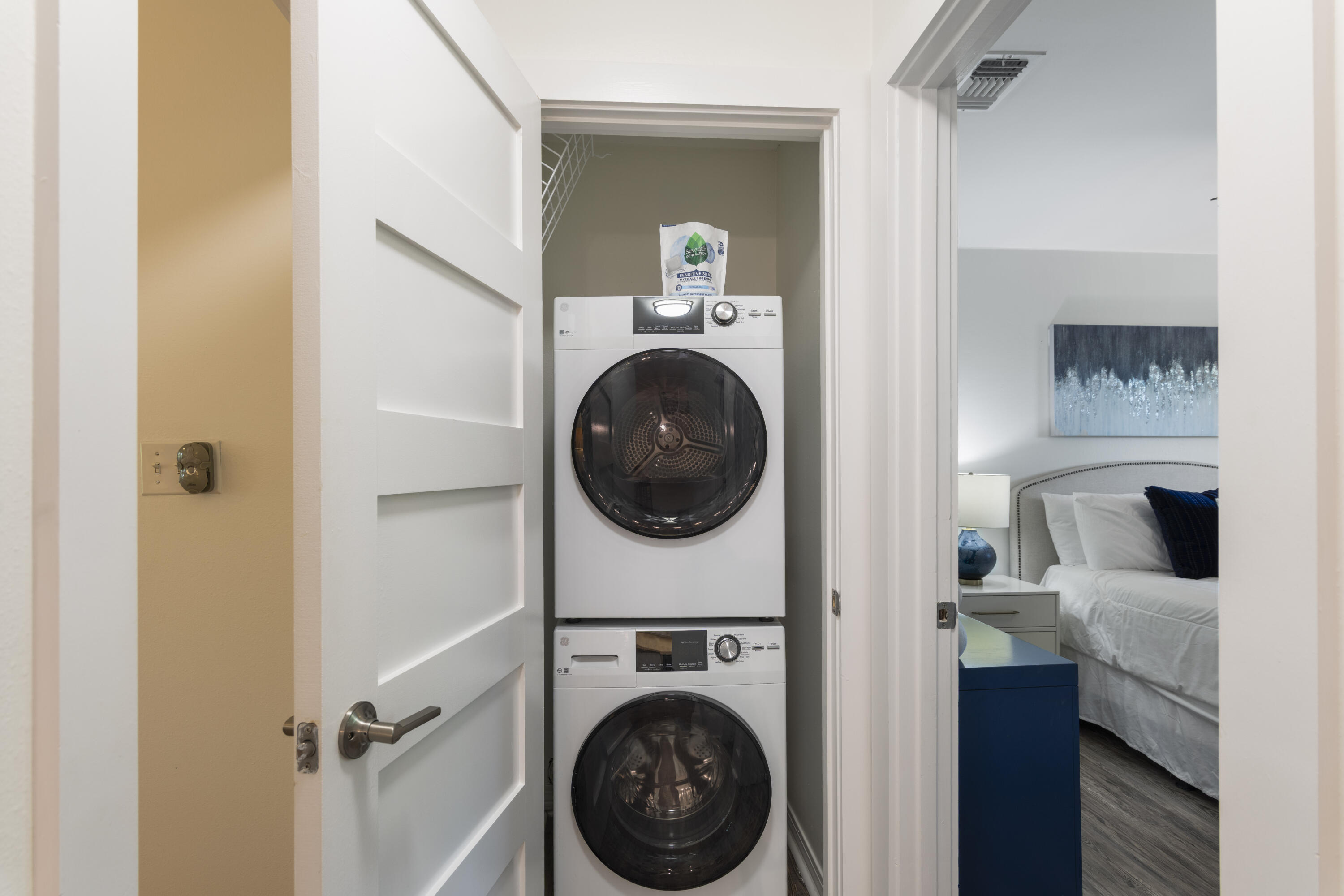 Stacked washer and dryer in a closet beside a bedroom with blue accents.