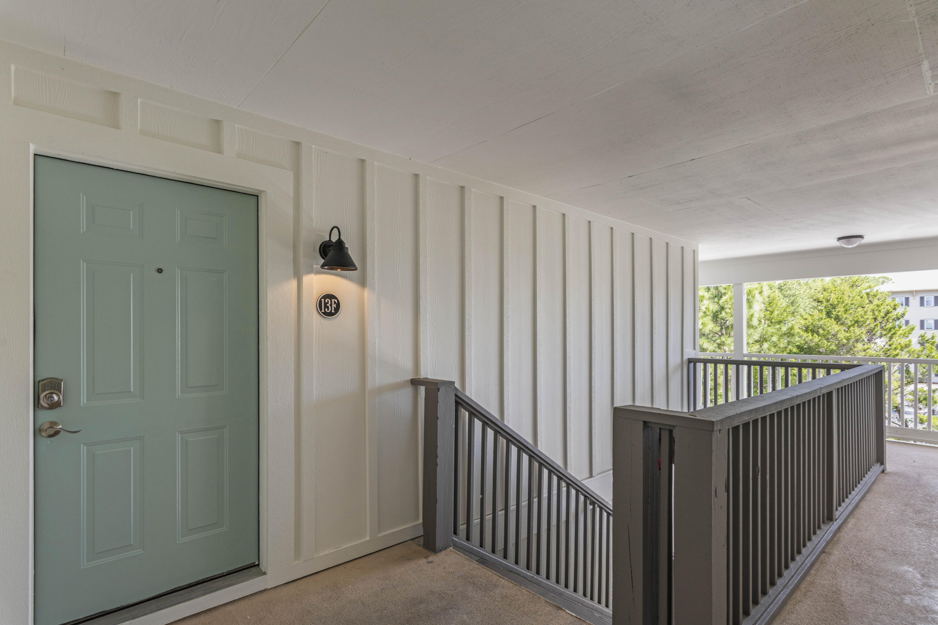 Condominium entry with a sage-green door marked 13F beside a covered walkway and dark railings.