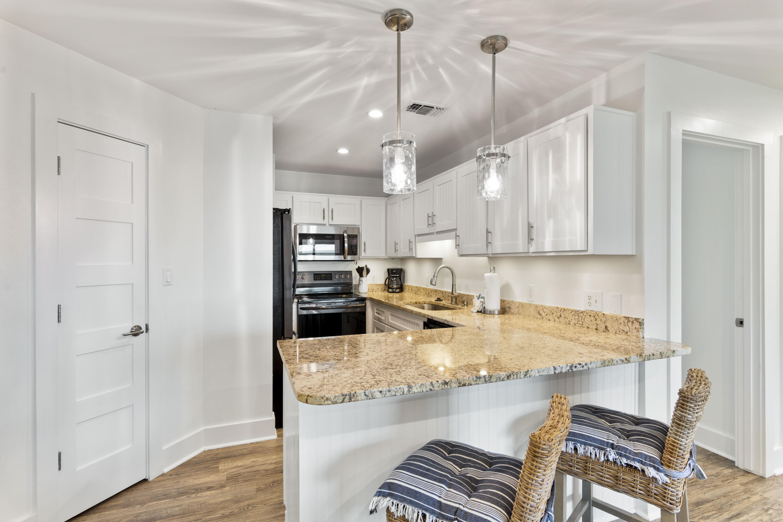 Kitchen with a large granite island, white cabinets, stainless steel appliances and wicker bar chairs.