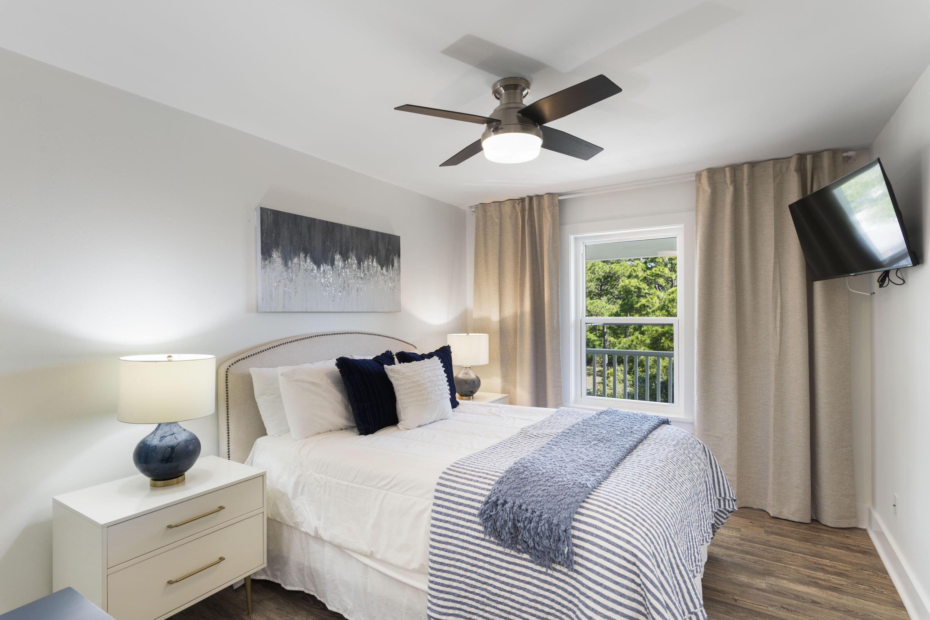 Furnished bedroom with striped bedding, blue accent pillows, and a window overlooking trees.