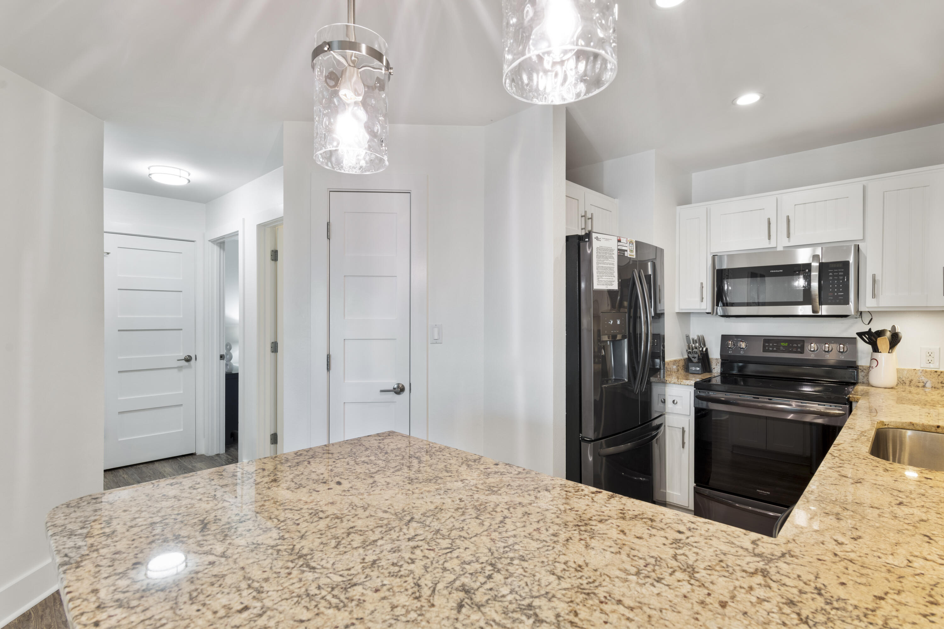 Kitchen with a granite island, white cabinets, black appliances, and glass pendant lights.