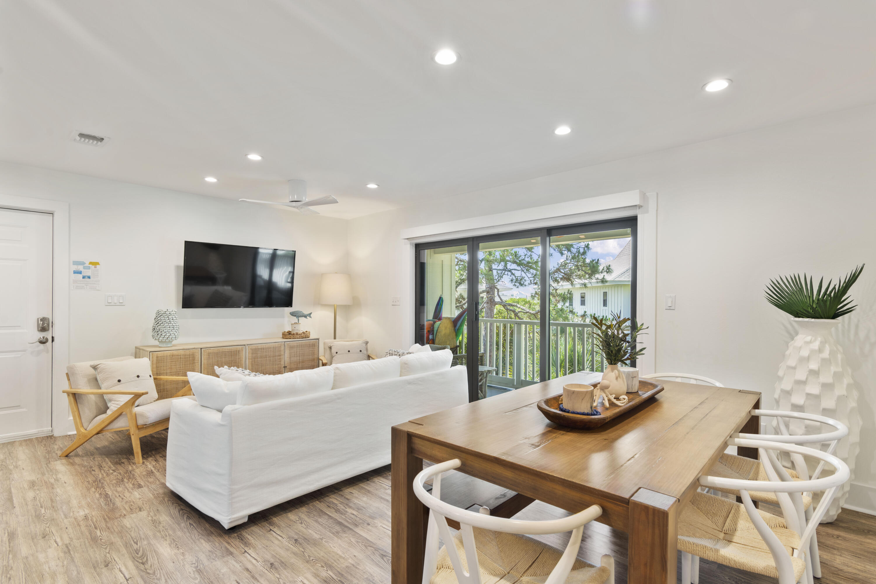 Living and dining room with white seating and a wooden table beside sliding doors overlooking a balcony and water.