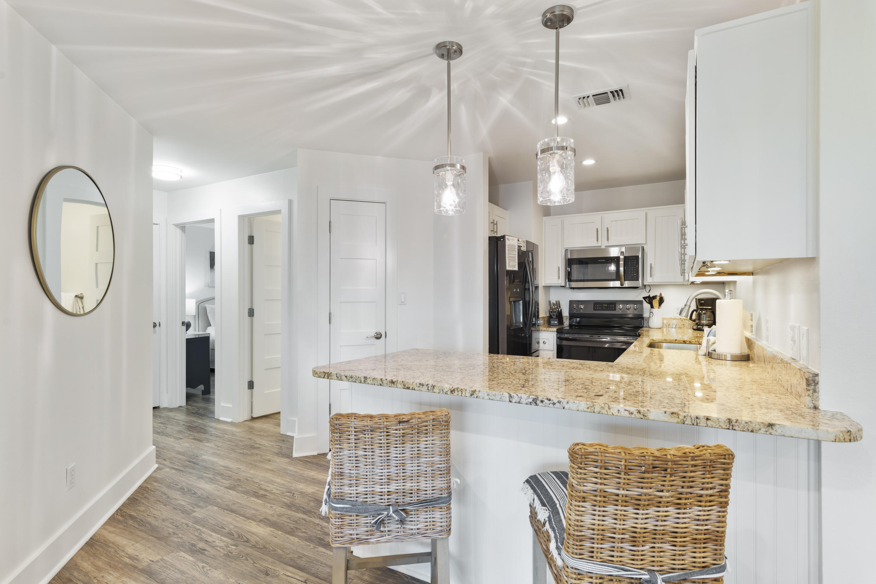 Kitchen with white cabinets, granite breakfast bar, woven stools, and black appliances.