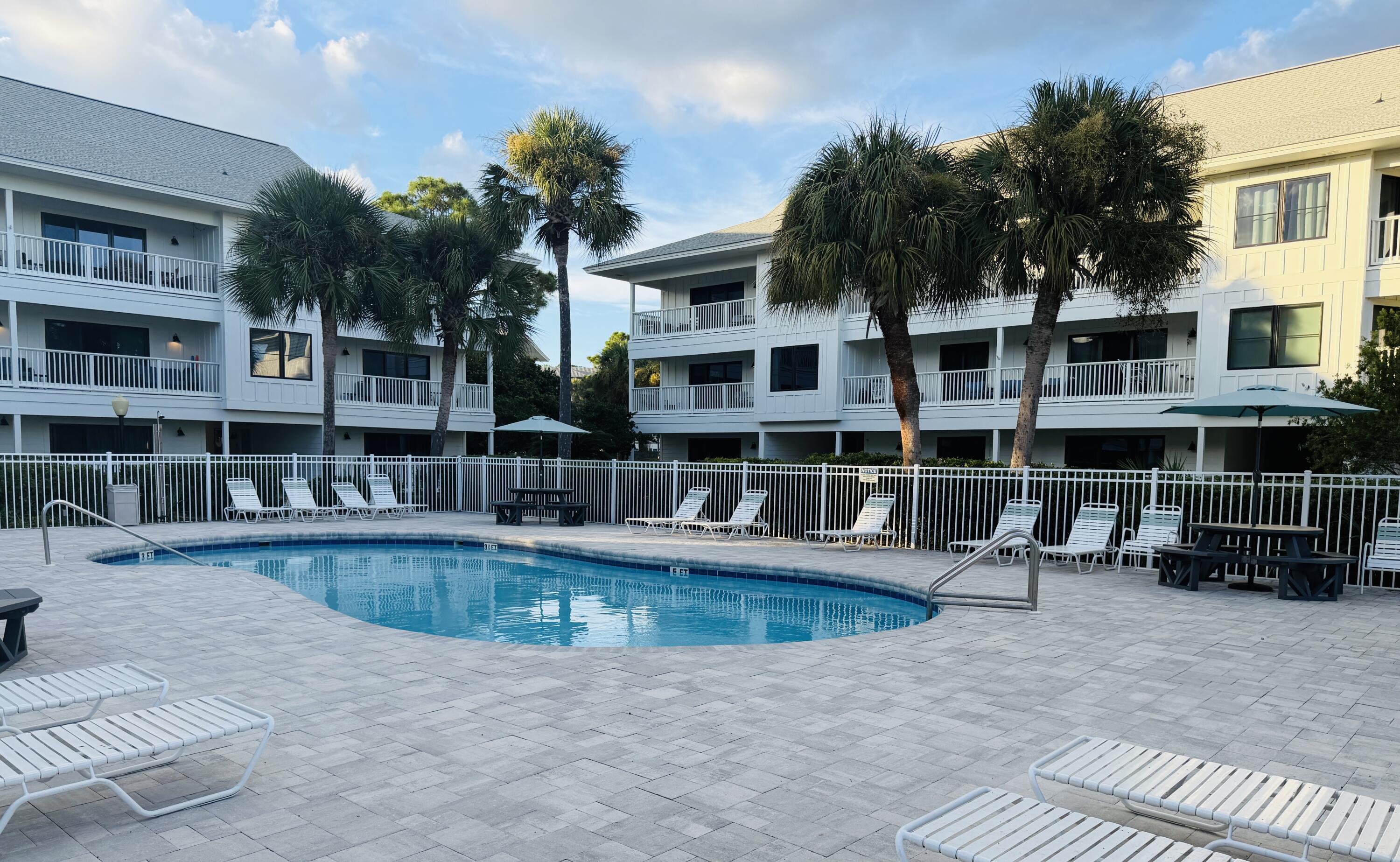 Outdoor pool with palm trees, lounge chairs, and white condominium buildings.