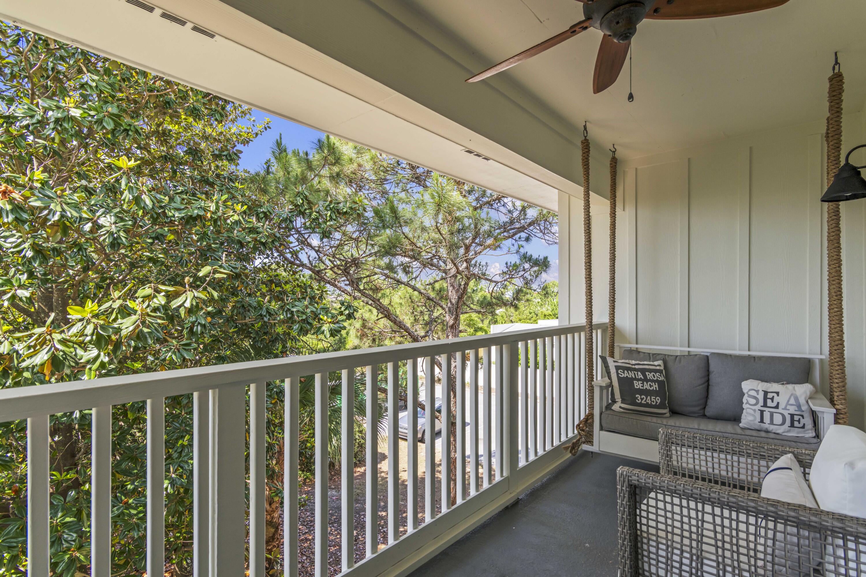 Covered balcony with a gray swing and wicker seating overlooking leafy trees.