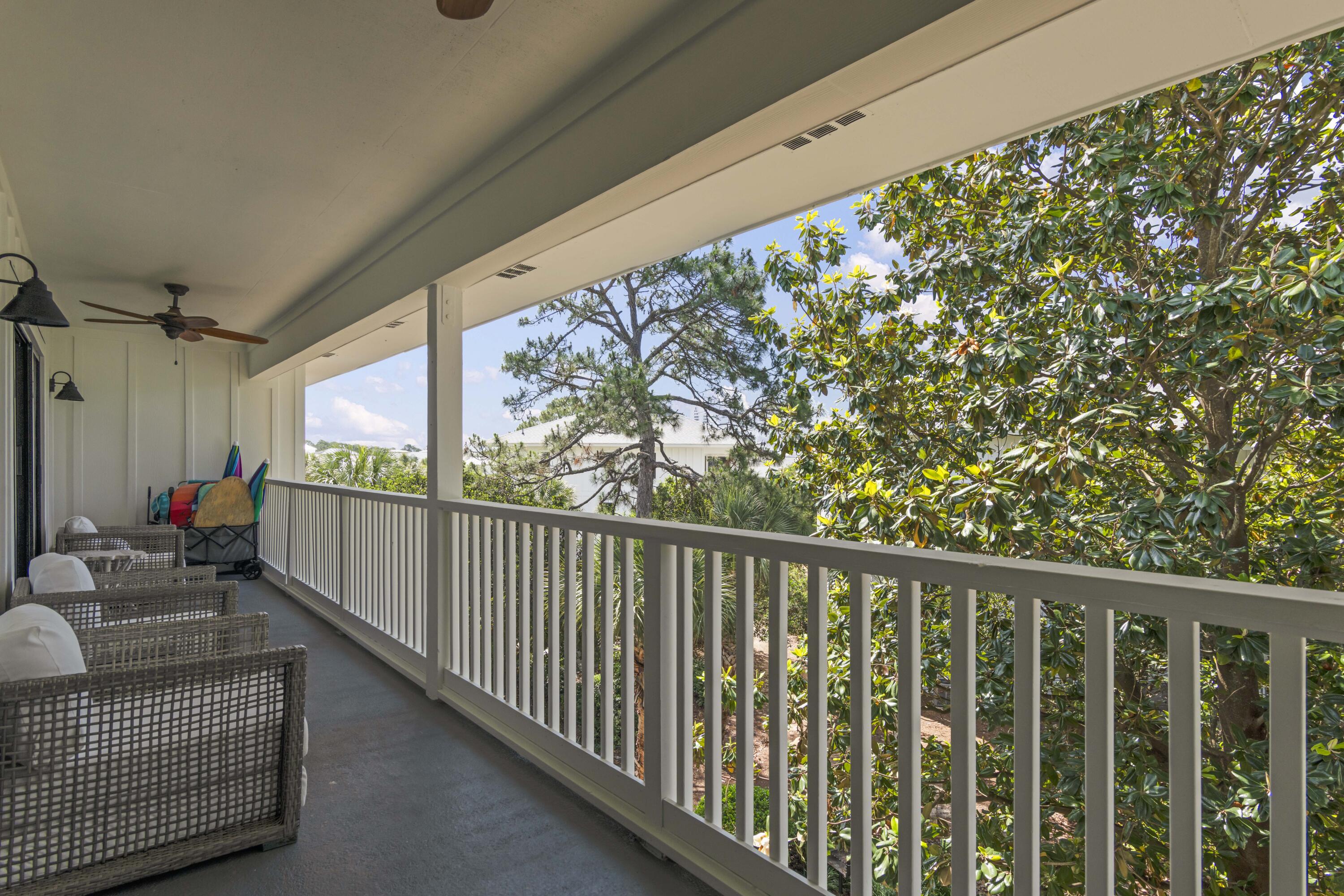 Covered balcony with wicker seating and a white railing overlooking leafy trees.