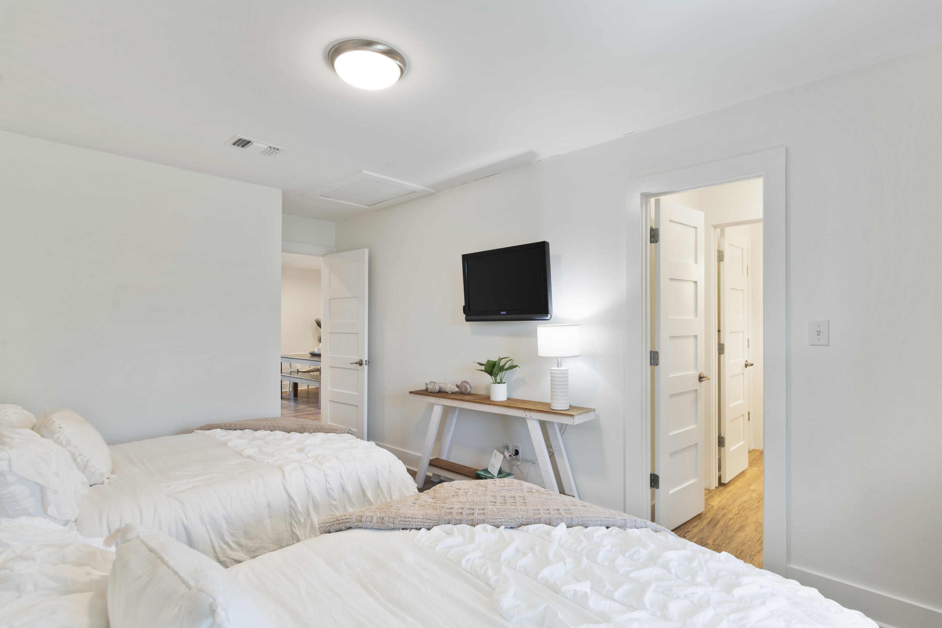 Bedroom with two white beds, a wall-mounted television, and open doorways to adjoining rooms.