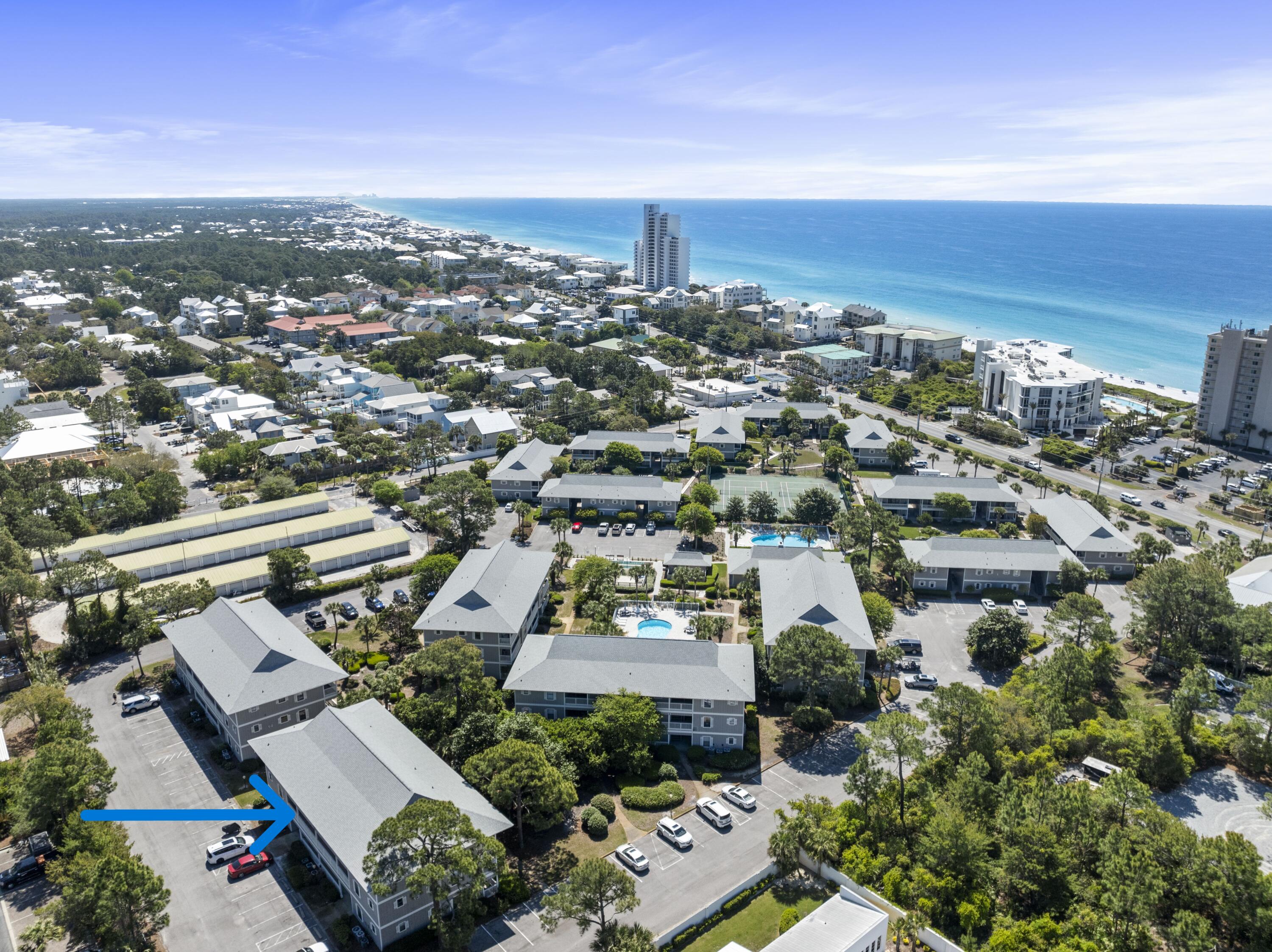 Aerial view of a coastal condominium complex, with a blue arrow pointing to one building and the Gulf in the distance.