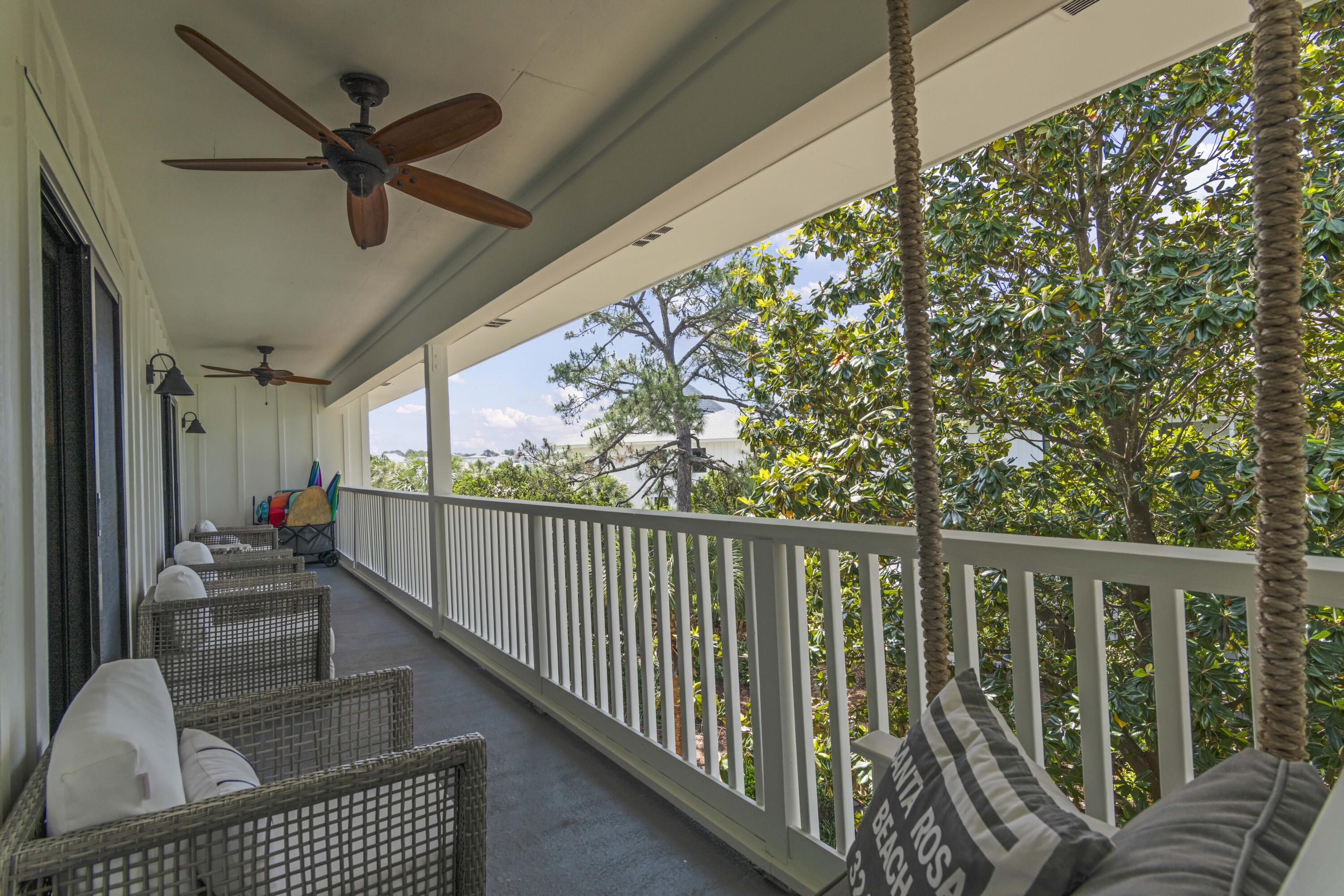 Covered balcony with wicker seating, ceiling fans, and leafy tree views.