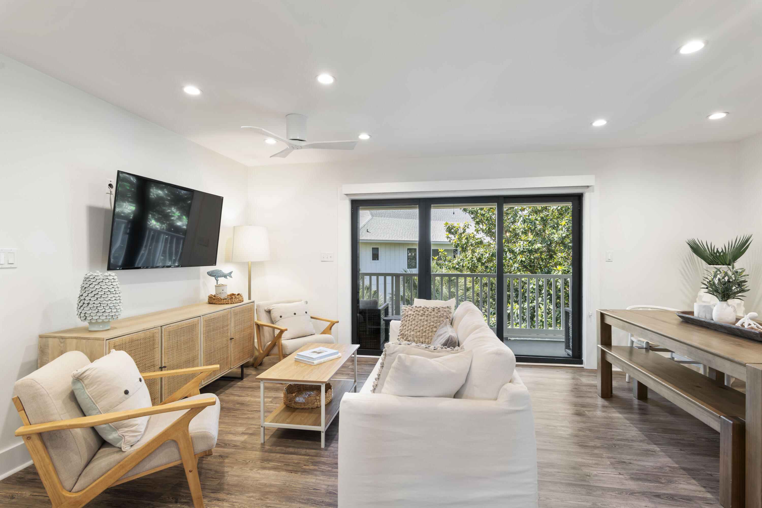 Furnished living room with white sofas and sliding glass doors opening onto a leafy balcony.