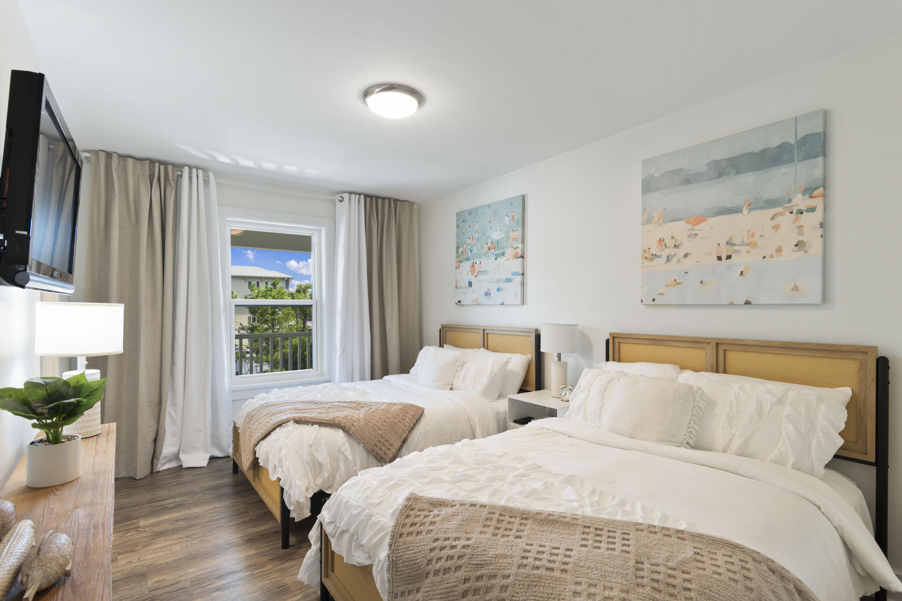 Bedroom with two white beds, woven wood headboards, and a window overlooking greenery.