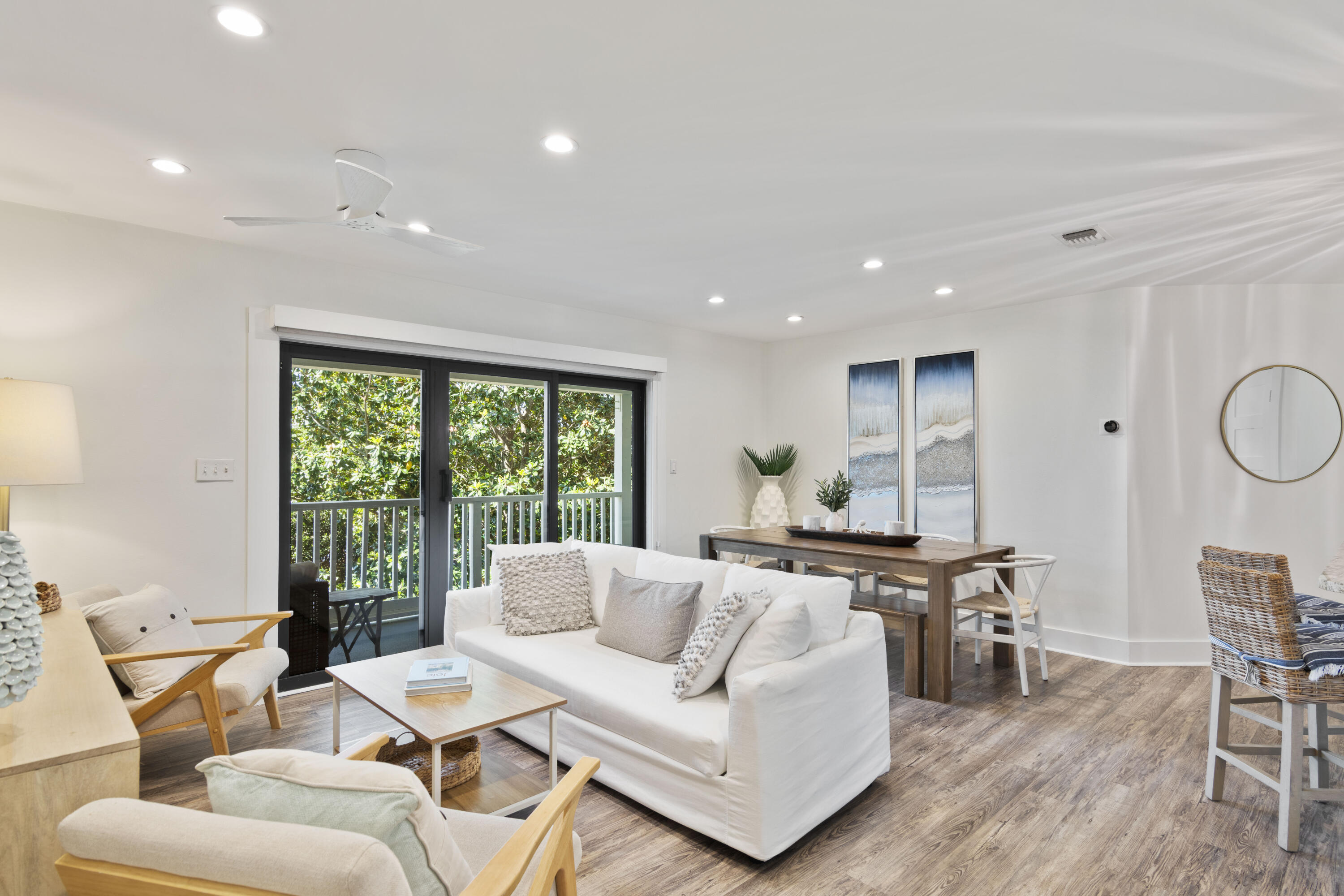 Open-plan living and dining room with white sofas and sliding glass doors overlooking leafy greenery.