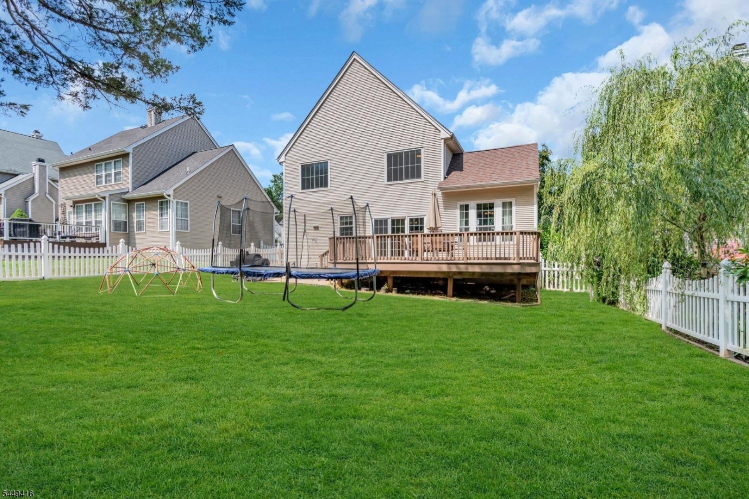 Rear of a two-story home with a raised deck, fenced lawn, trampoline, and climbing dome.