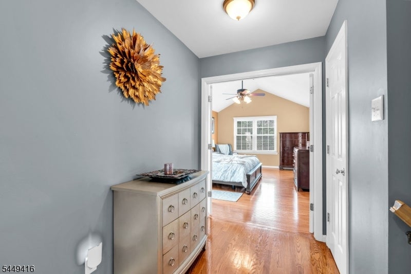 Hallway opening into a bedroom, with hardwood floors and a light-colored chest in the foreground.