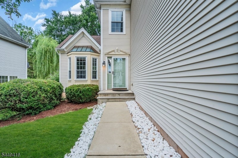 House entrance with a stone-bordered walkway, bay windows, and landscaped shrubs.