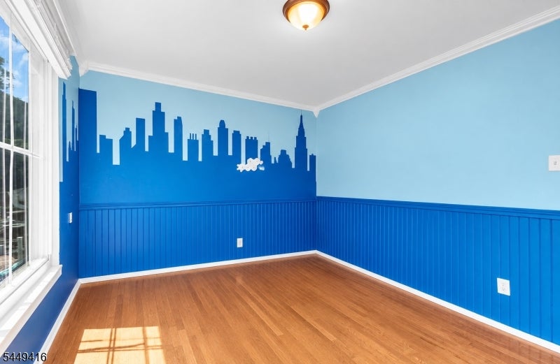 Empty blue room with a skyline mural, paneled walls, hardwood floors, and a large window.