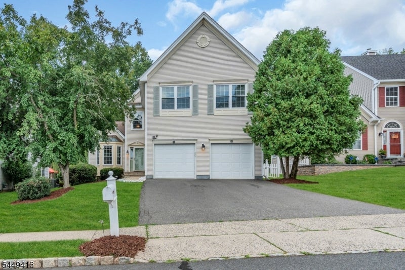 Beige two-story home with a front gable, double garage, driveway, and mature trees.