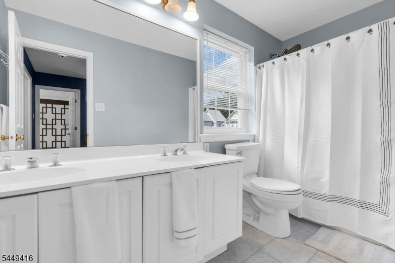 Bathroom with a long white vanity, mirrored wall, and white shower curtain with dark trim.