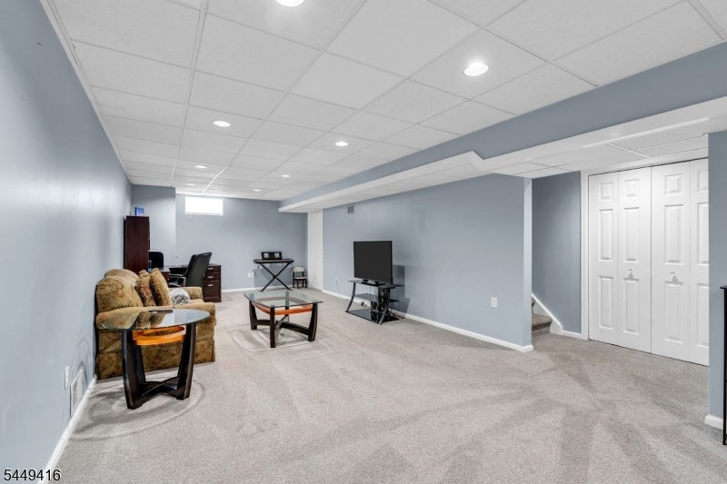 Furnished basement recreation room with a sofa, television, carpet, and white closet doors.
