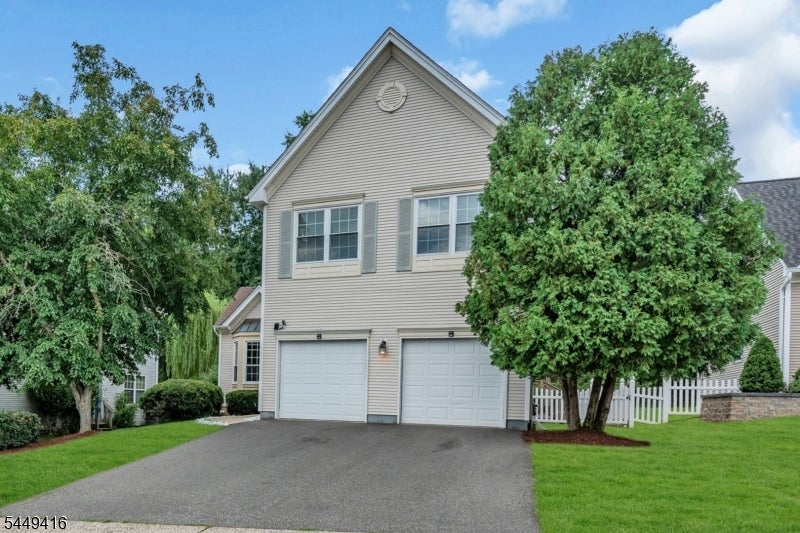 Two-story beige house with a double garage, broad driveway, and mature trees.