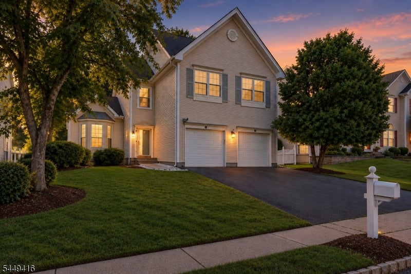 Two-story home at dusk with a front gable, double garage, mature trees, and a white mailbox.
